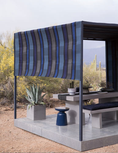 一张亚利桑那州沙漠地带的户外照片，画面中以 Sunbrella 遮阳织物覆盖搭成的现代凉棚内有一张餐桌和几张长凳。
