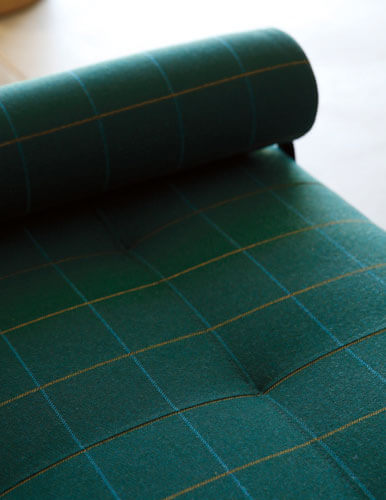 Close-up of a sofa cushion and armrest, covered in dark green checked Sunbrella upholstery fabric.