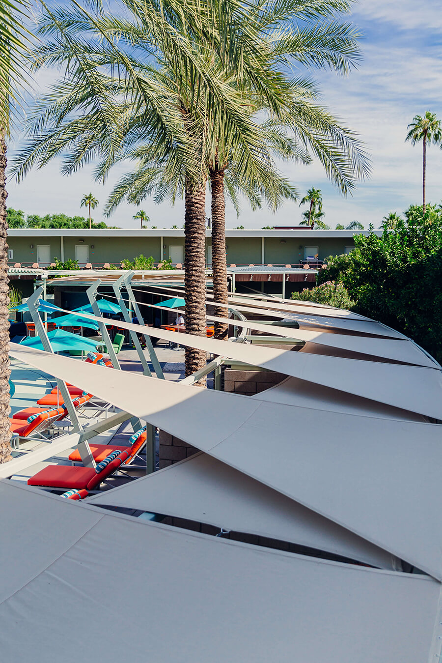 Shade Sail Installation Poolside Shade sail with beige Sunbrella Contour fabric installed at hotel pool with palm trees in background