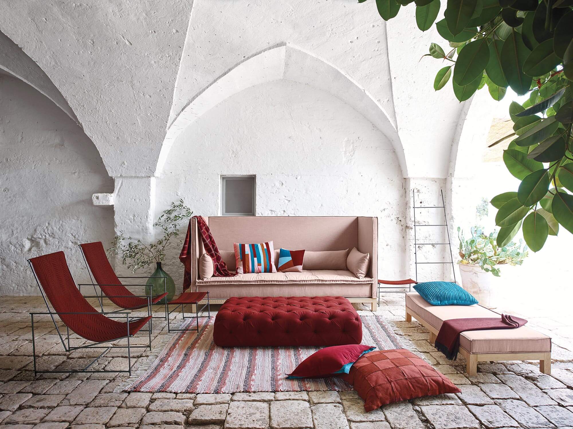 A living room with a large sofa, chairs, and a tufted ottoman in hues of red and pink are made using Sunbrella upholstery fabric