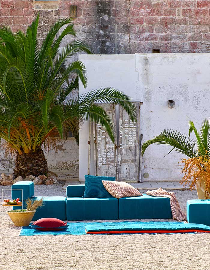 Teal seating cushions with palm trees and brick wall background.